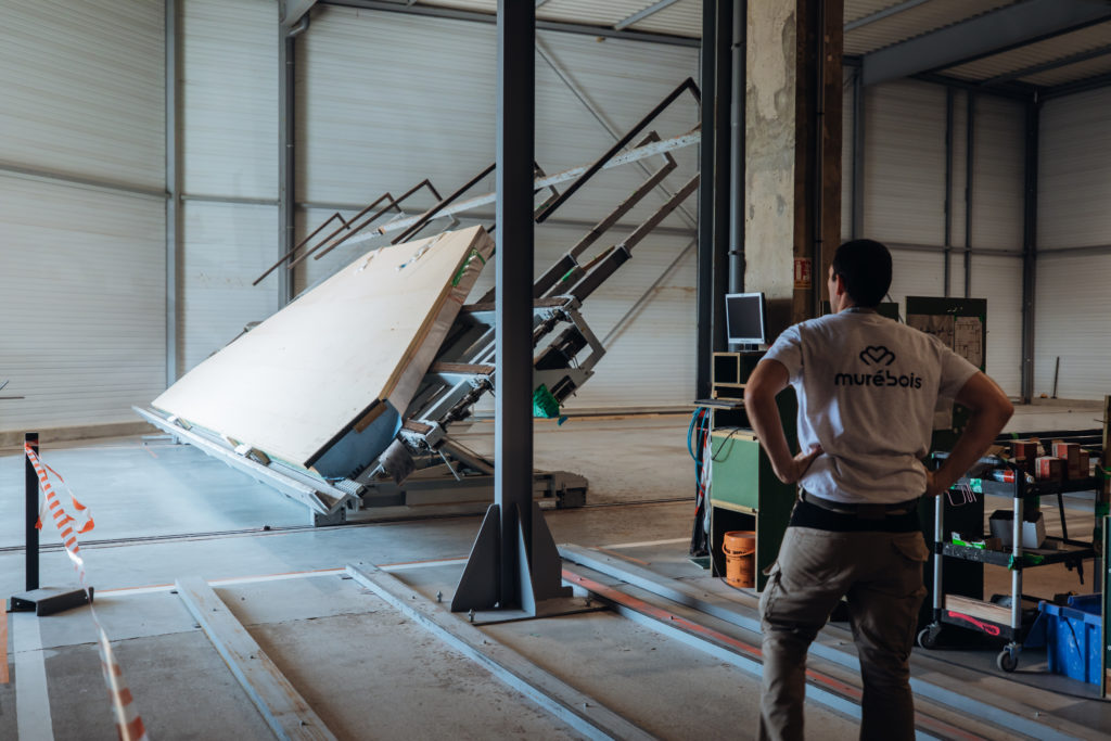 Machine qui soulève une façade de maison en bois avec un collaborateur Murébois qui surveille la manoeuvre.